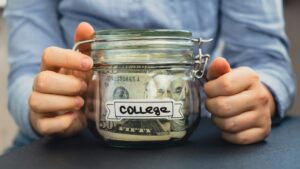 Unrecognizable woman holding Saving Money In Glass Jar filled with Dollars banknotes. COLLEGE
