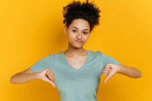 Negative pessimistic young african american woman with curly hair, dressed in basic t-shirt, showing
